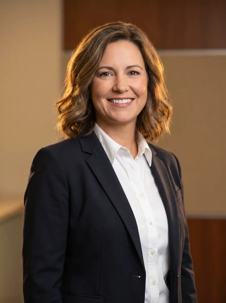 Corporate headshot in a crisp white shirt and dark blazer, warm neutral background, soft rim light, confident approachable smile